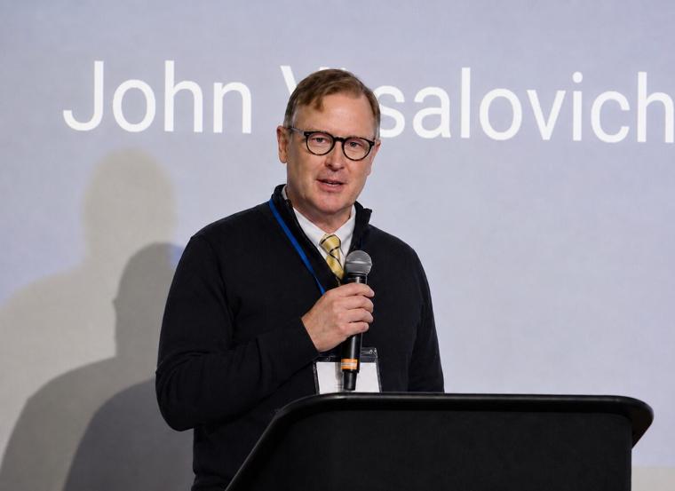 John Vrsalovich speaking at a podium with a microphone